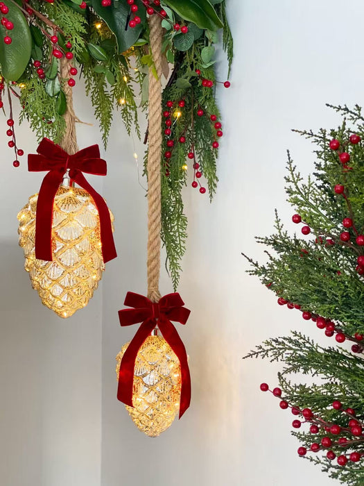 Illuminated mercury glass pinecone ornaments in two sizes styled with red velvet bows