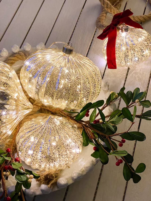 Close-up of illuminated mercury glass onion ornaments styled with Christmas greenery