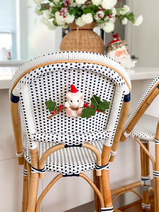 Felt hanging mouse ornament with green leaves and red berries on a woven chair