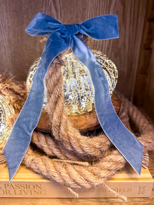 Close-up of an illuminated mercury glass onion ornament styled with rope and a blue velvet bow