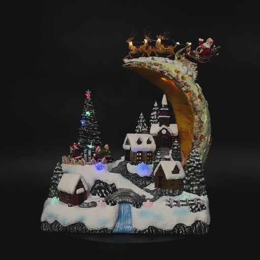 Illuminated Christmas village beneath Santa's moonlit sleigh in motion